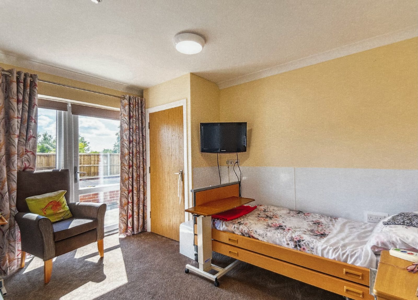A single bedroom at Stronvar with an armchair, television and patio doors onto the courtyard
